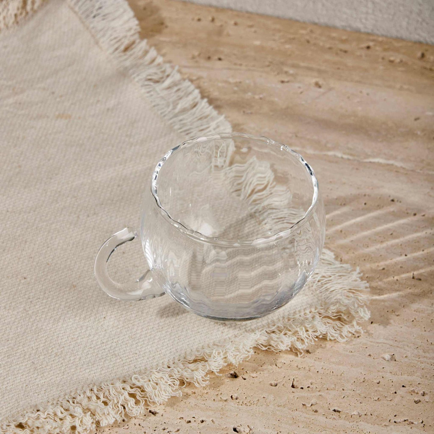 Transparent glass KURE CUP with ergonomic handle on textured fabric background.