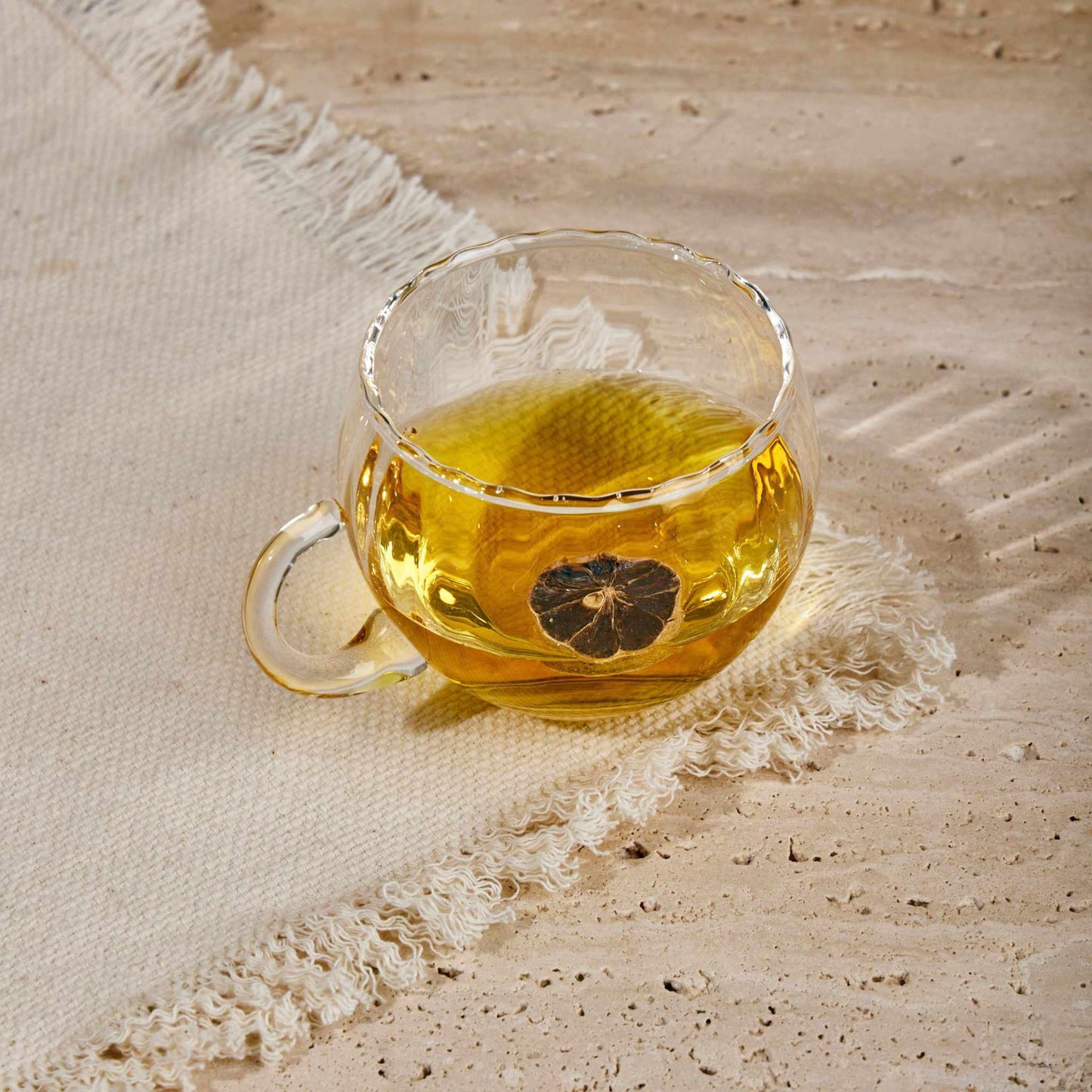 Transparent KURE CUP with ergonomic handle showcasing tea, resting on a textured surface.