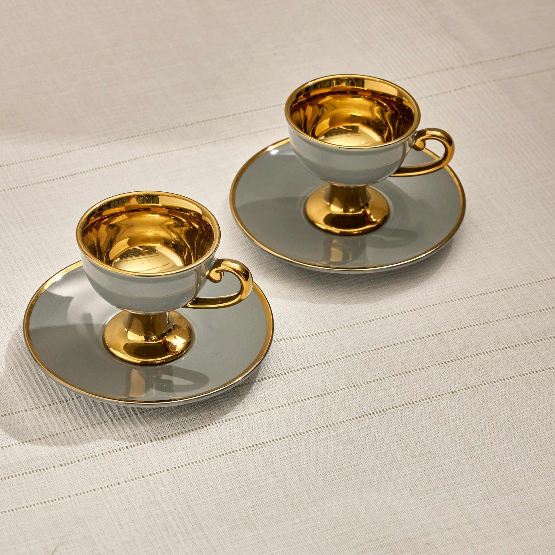 Lalia Cup Gray Set of 2 with matte gray exterior and gold interior on saucers.