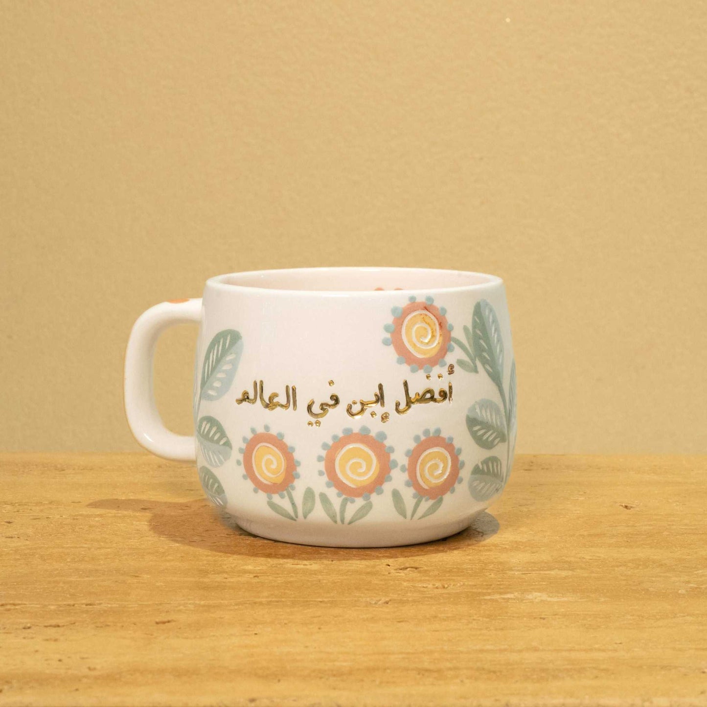 Personalized gold Arabic monogram ceramic mug with "Best Son in the World" and floral design.