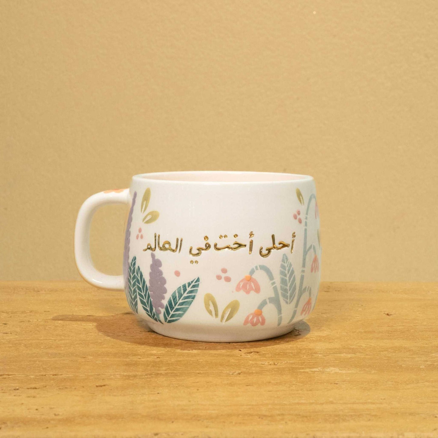 Personalized ceramic mug with gold Arabic monogram "Best Sister in the World" and floral design.