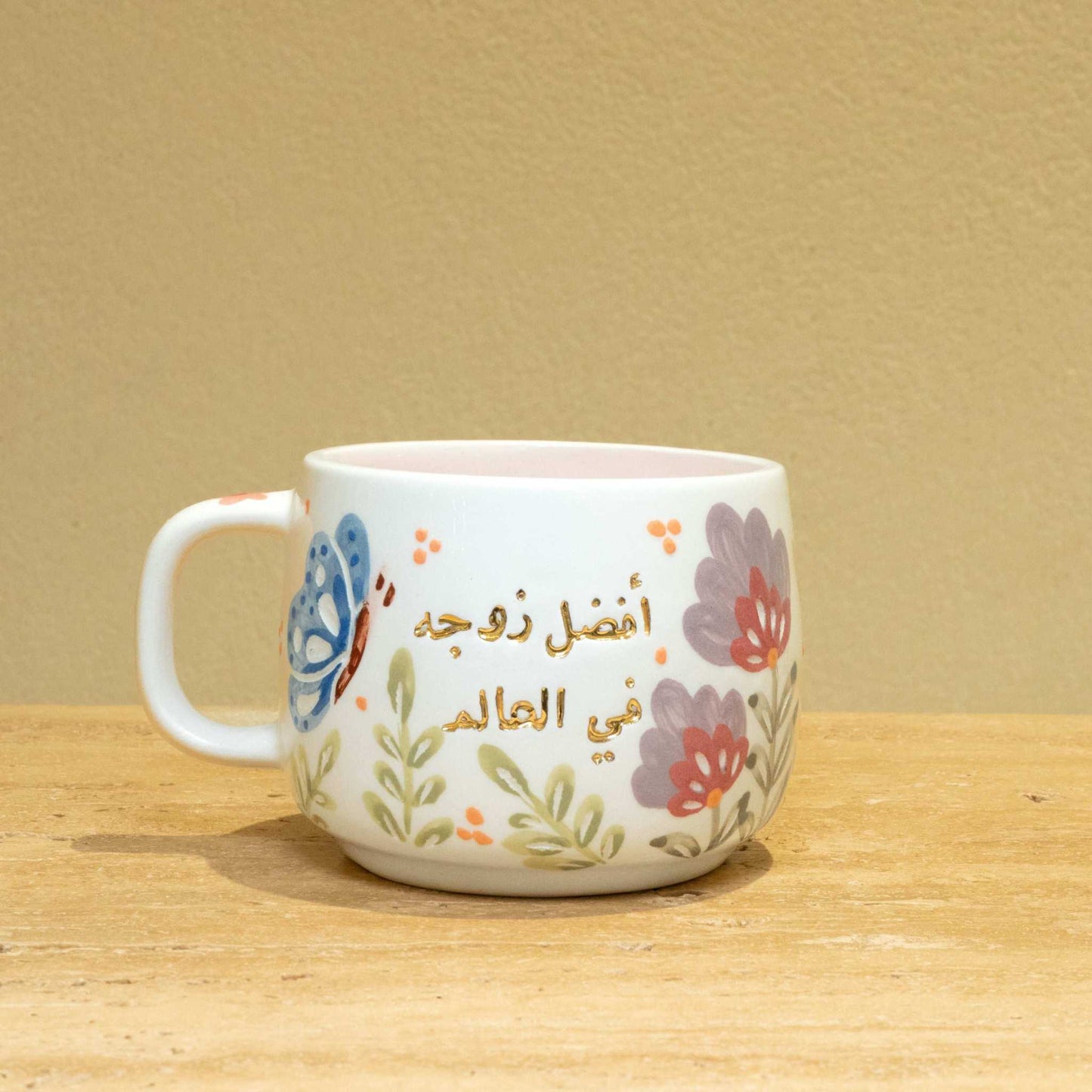 Handmade ceramic mug with gold Arabic script "Best Wife In The World (أفضل زوجة في العالم)" and floral design.