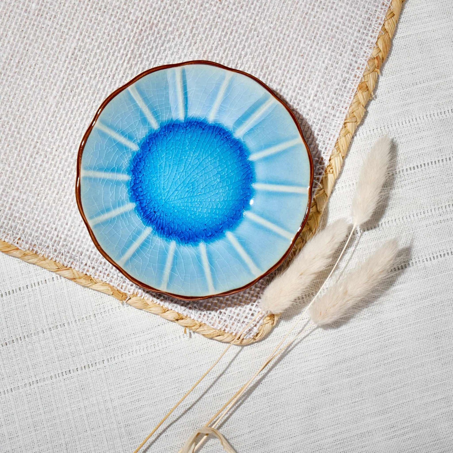 ACEM Ceramic Tea Plate in blue with sunburst design and textured center on woven placemat.