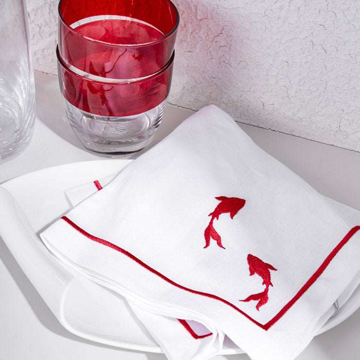 White linen placemat and napkin set with red fish embroidery and picot edging.