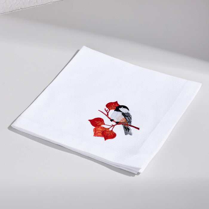 White linen cocktail napkin with embroidered bird and autumn leaves design.
