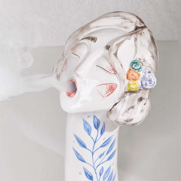 Ceramic handmade colorful girl face incense burner with floral accents.