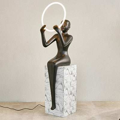 Meditation sculptural floor lamp with black human figure and LED ring on a marble-like pedestal.