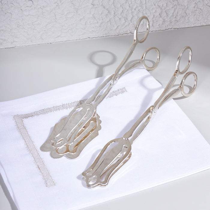 Plated scissor cake server in silver on a white napkin.
