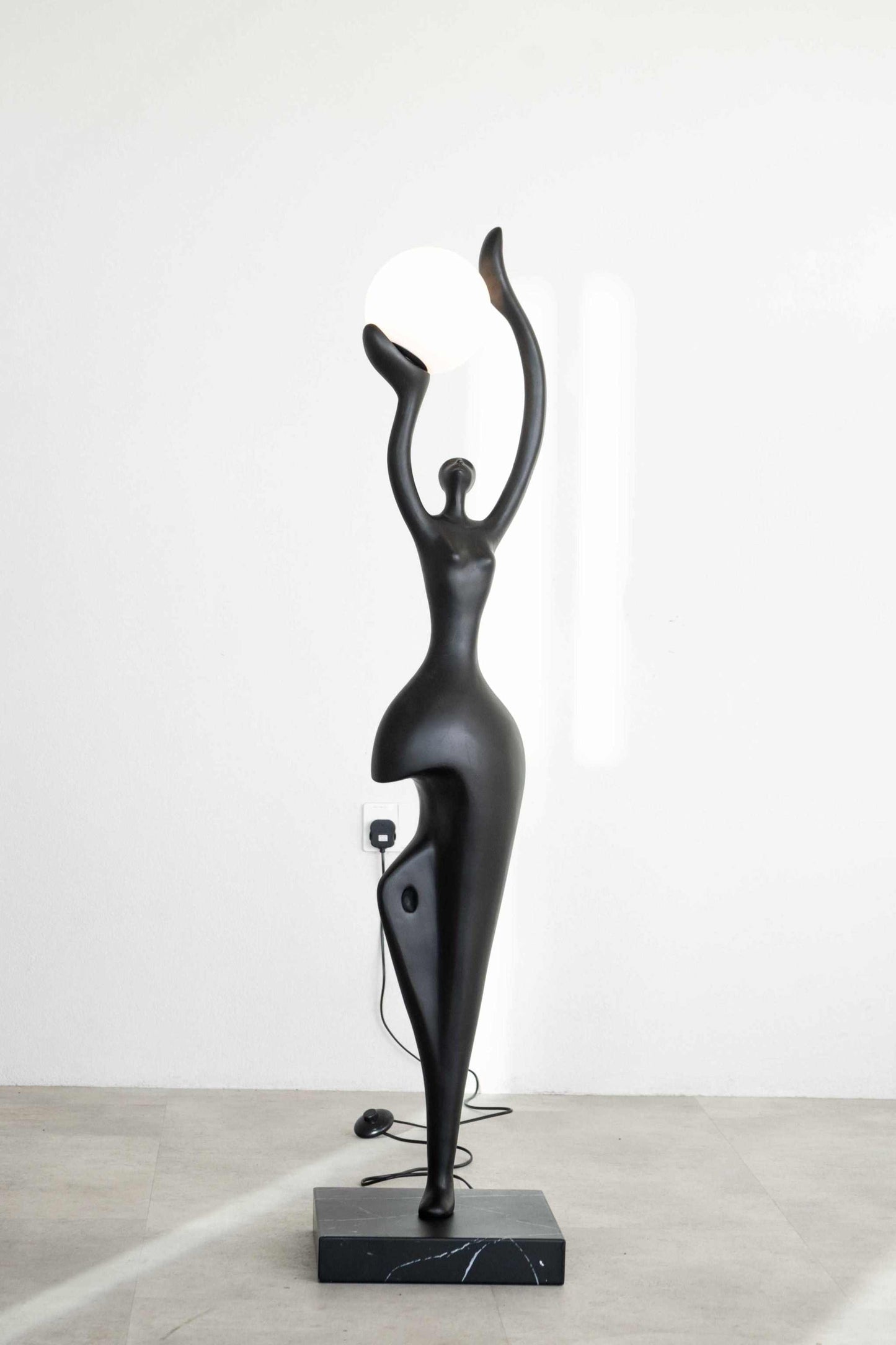 Lady Liberty Sculptural floor lamp in matte black with abstract human form holding a glowing globe on a metal base.