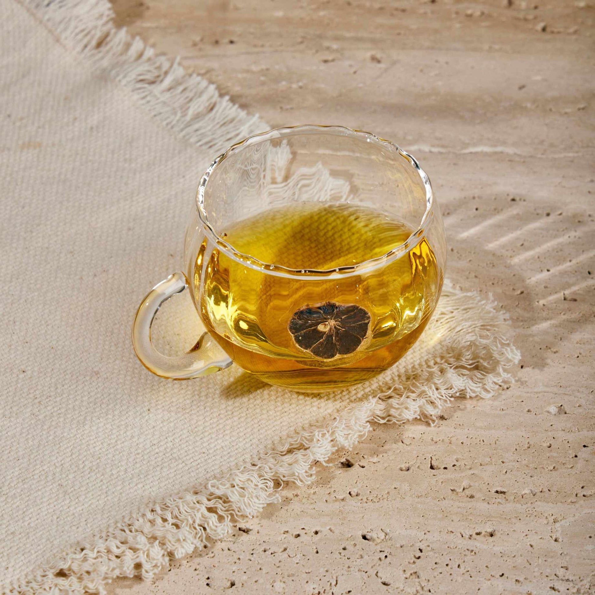 Transparent KURE CUP with ergonomic handle showcasing tea, resting on a textured surface.