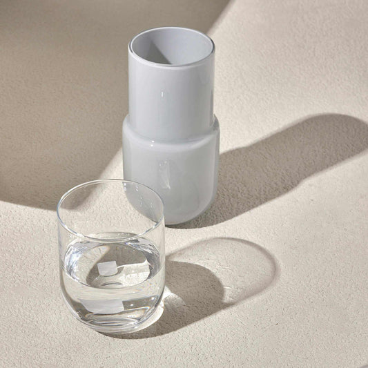 Sleek white water night set with carafe and glass on bedside table.
