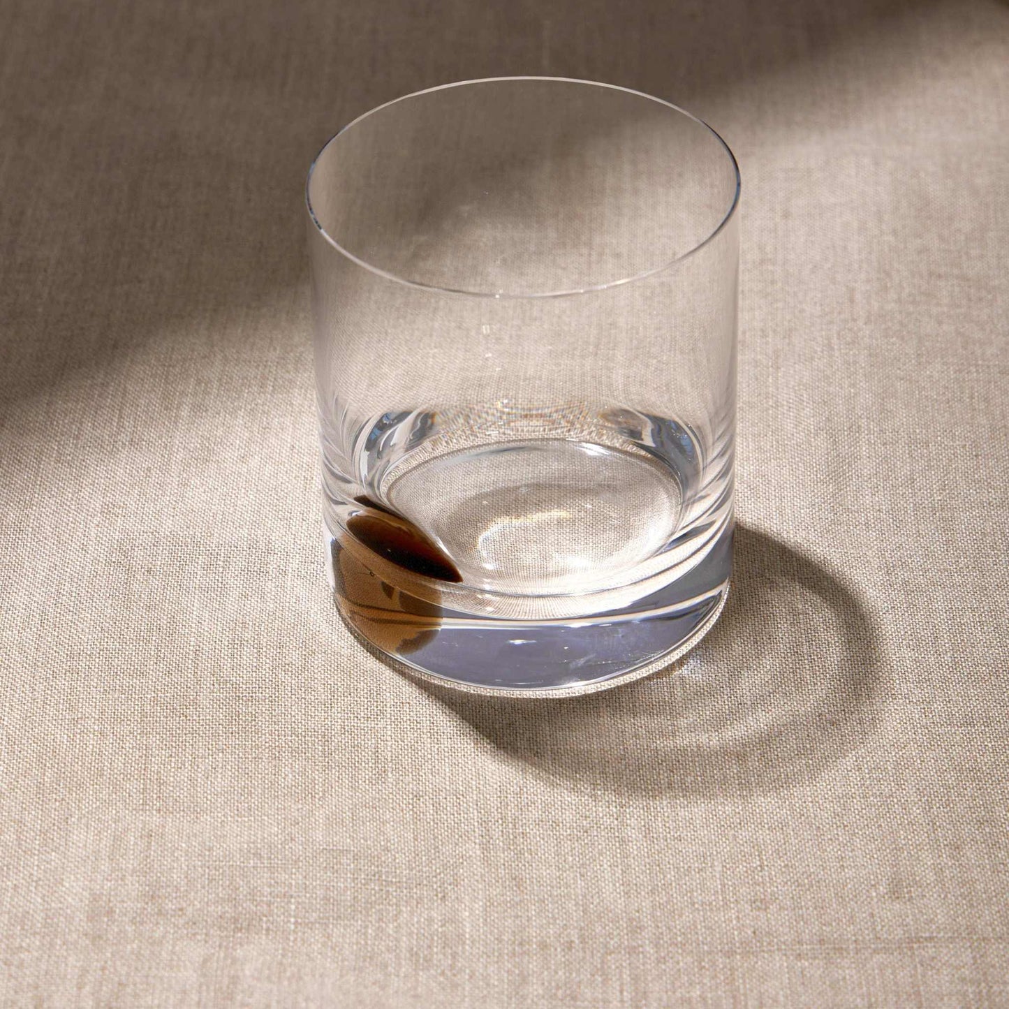 DOT WHISKEY GLASS - AMBER with unique spinning base on a textured surface.
