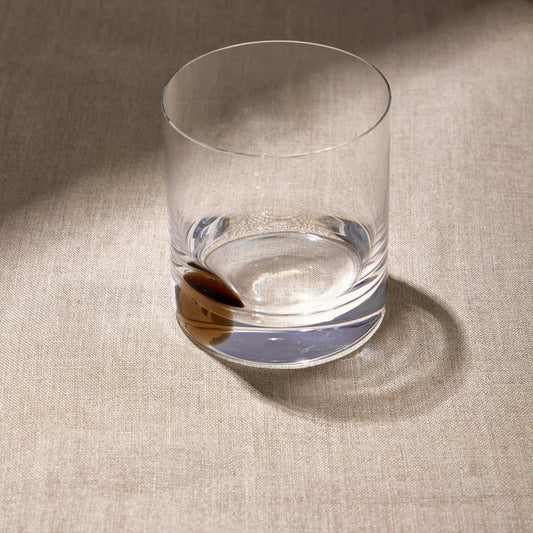 DOT WHISKEY GLASS - AMBER with unique spinning base on a textured surface.