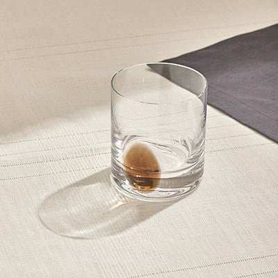 DOT WHISKEY GLASS - CARAMEL on table, designed for a sophisticated whiskey-drinking experience with a unique spinning base.