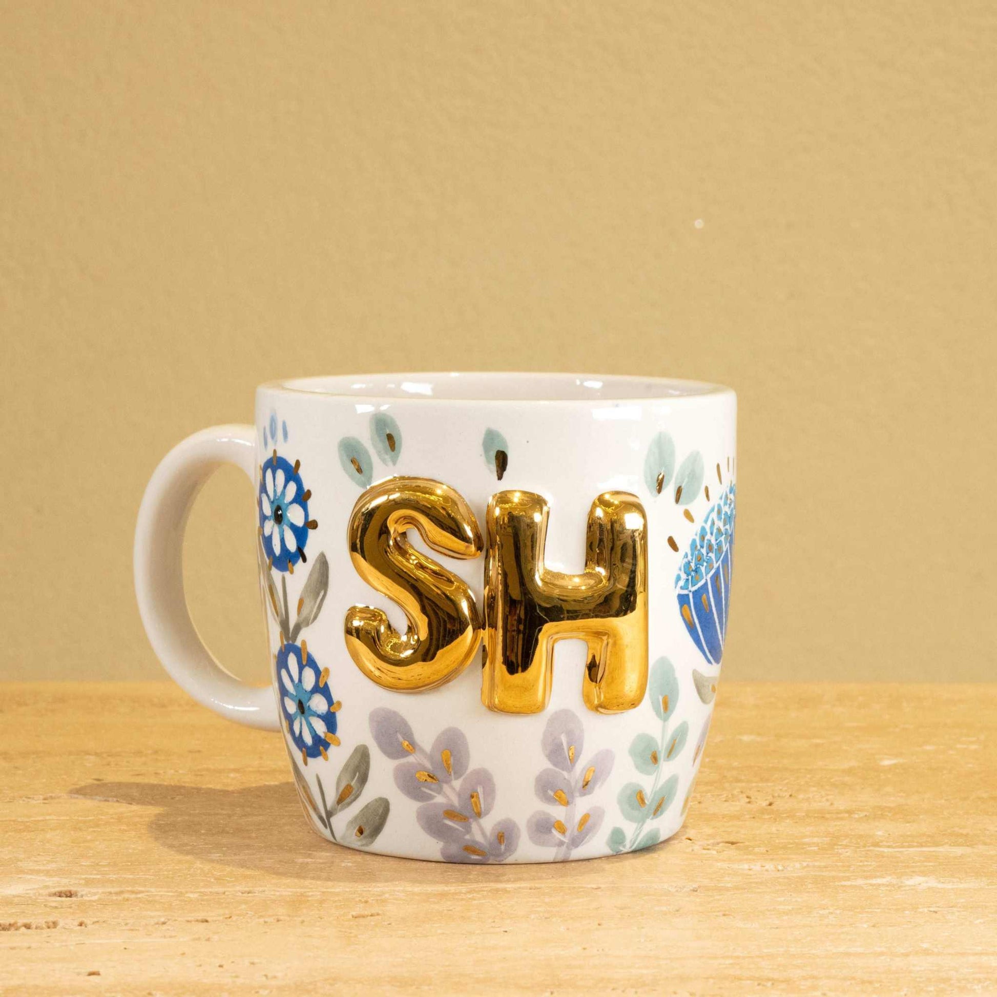 Personalized handmade ceramic mug with gold-plated "SH" letters and floral design.