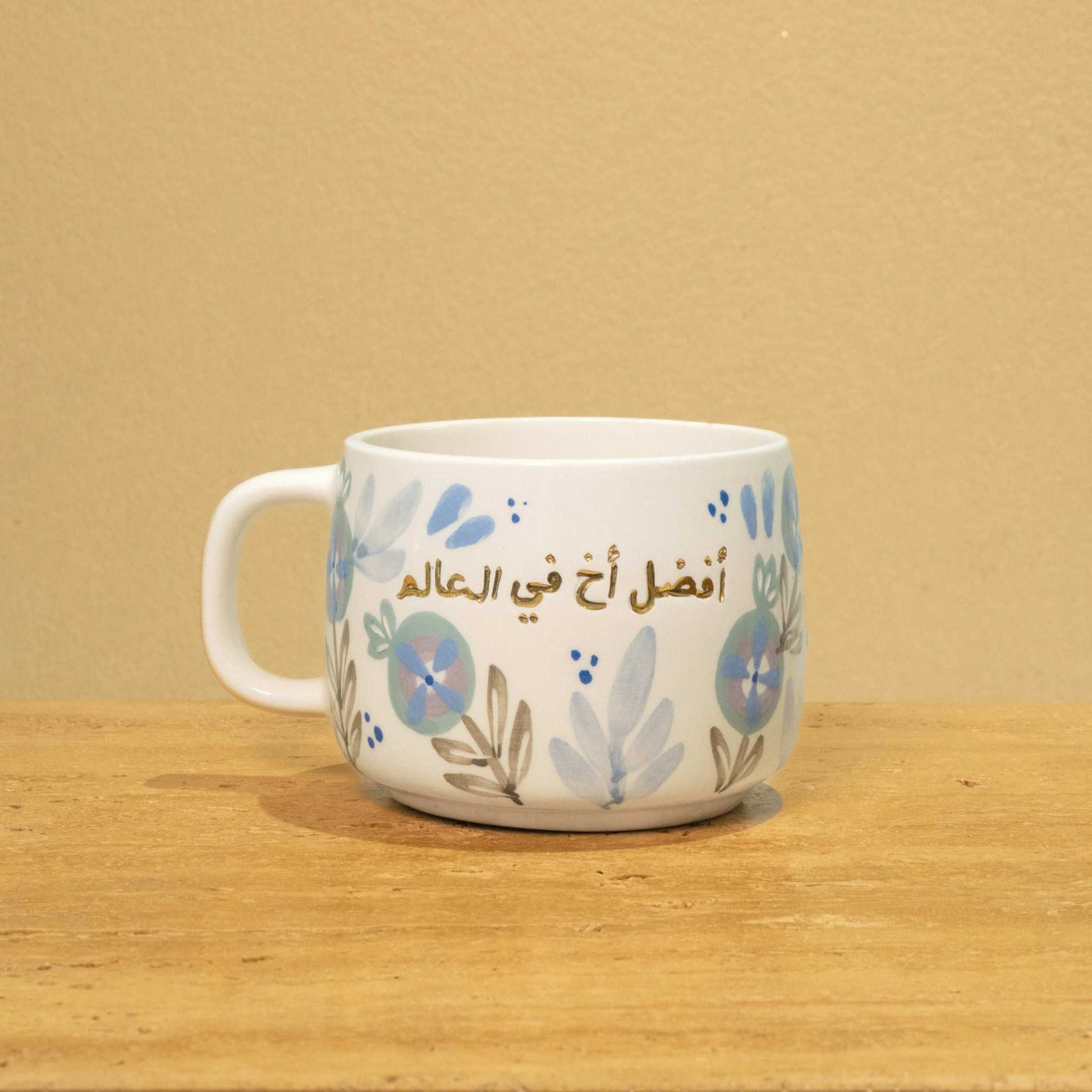 Personalized gold Arabic monogram ceramic mug with floral design, reading "Best Brother in the World".