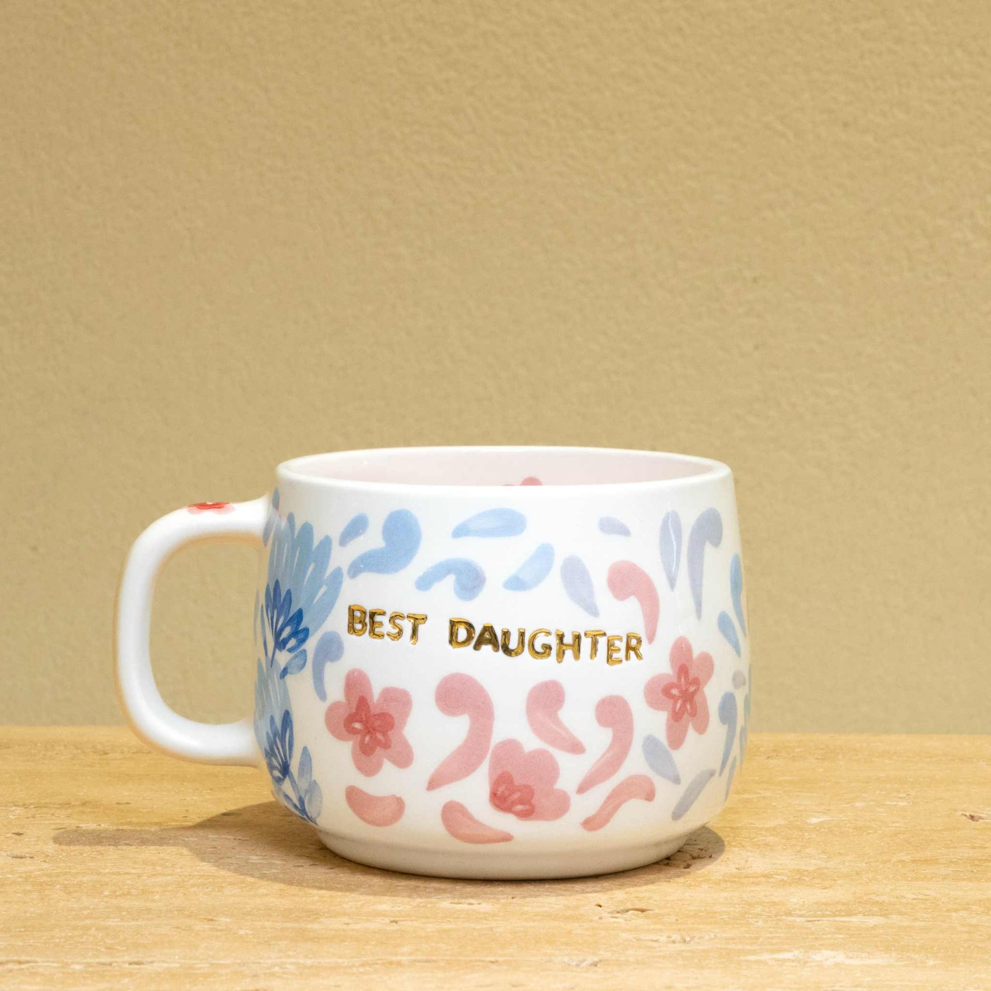 Personalized gold monogram ceramic mug with "Best Daughter" and floral design.
