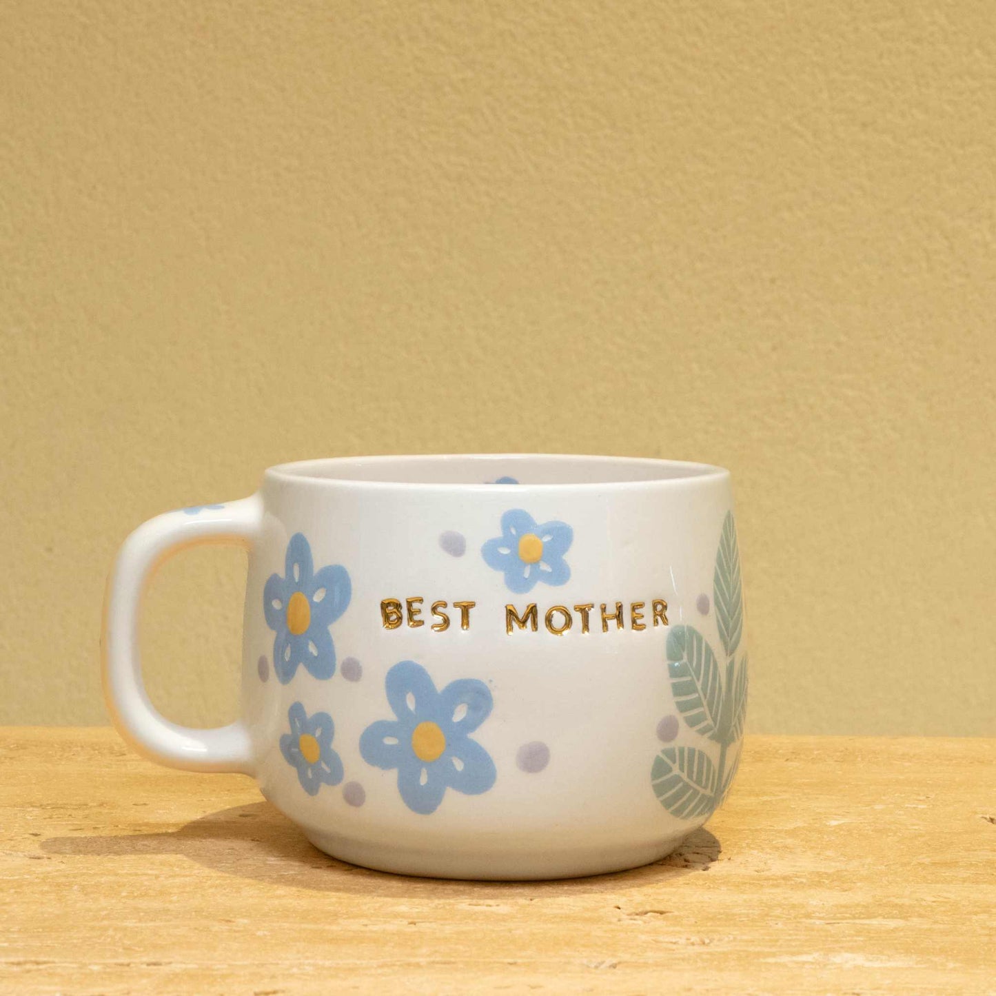 Personalized gold monogram ceramic mug with "Best Mother" and floral design.