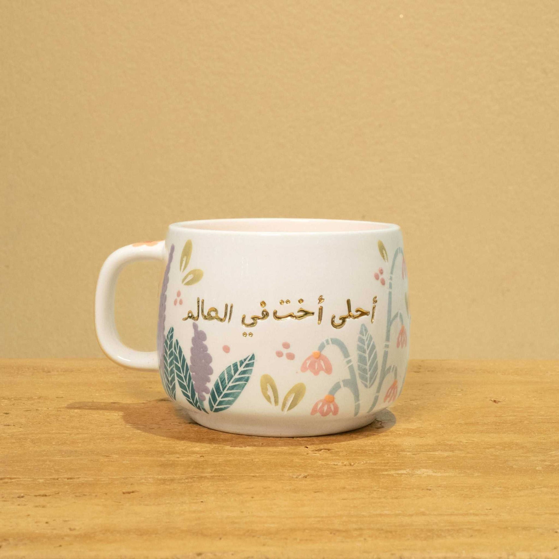 Personalized ceramic mug with gold Arabic monogram "Best Sister in the World" and floral design.
