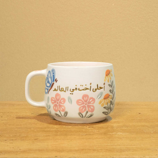Gold Arabic monogram ceramic mug with floral design, "Best Sister in the World".
