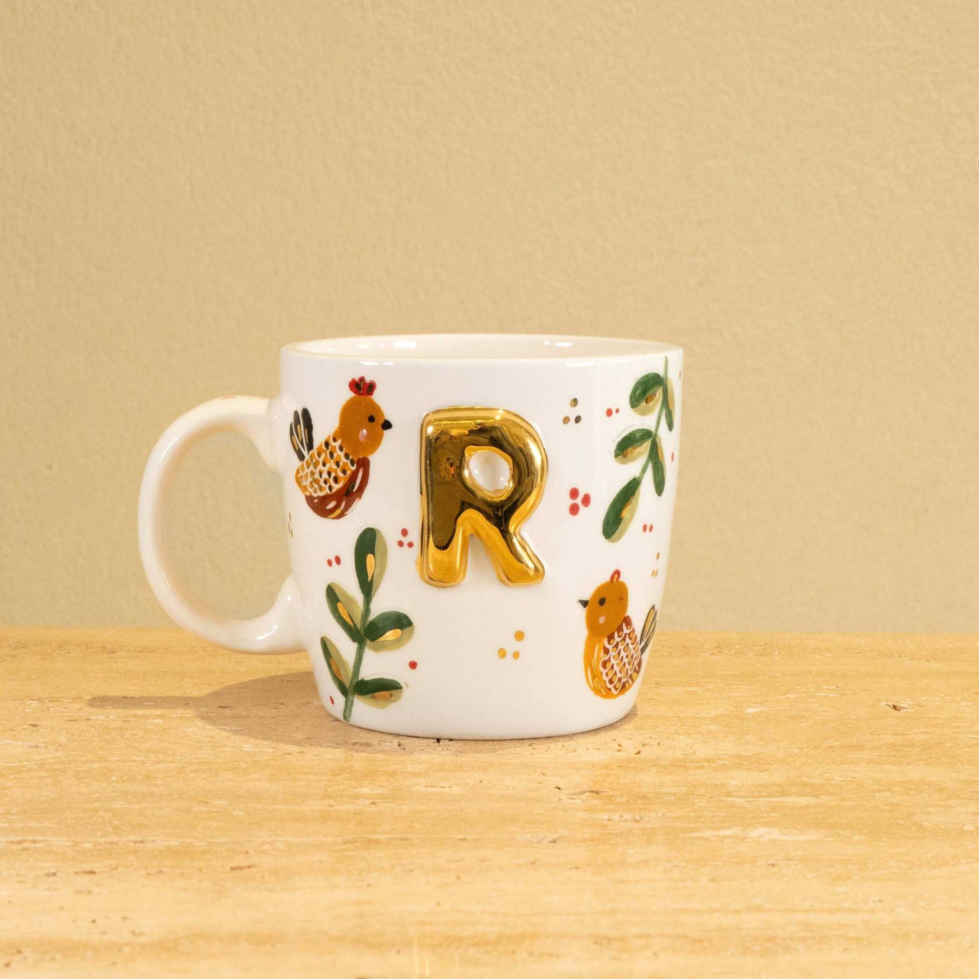 Custom handmade ceramic mug with gold-plated initial "R" and floral design.