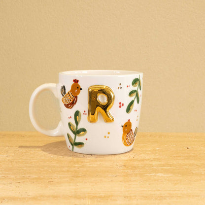 Custom handmade ceramic mug with gold-plated initial "R" and floral design.