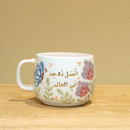 Handmade ceramic mug with gold Arabic script "Best Wife In The World (أفضل زوجة في العالم)" and floral design.