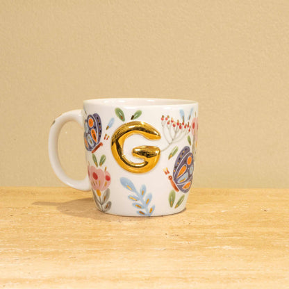 Custom handmade ceramic mug with gold-plated initial "G" and floral design.