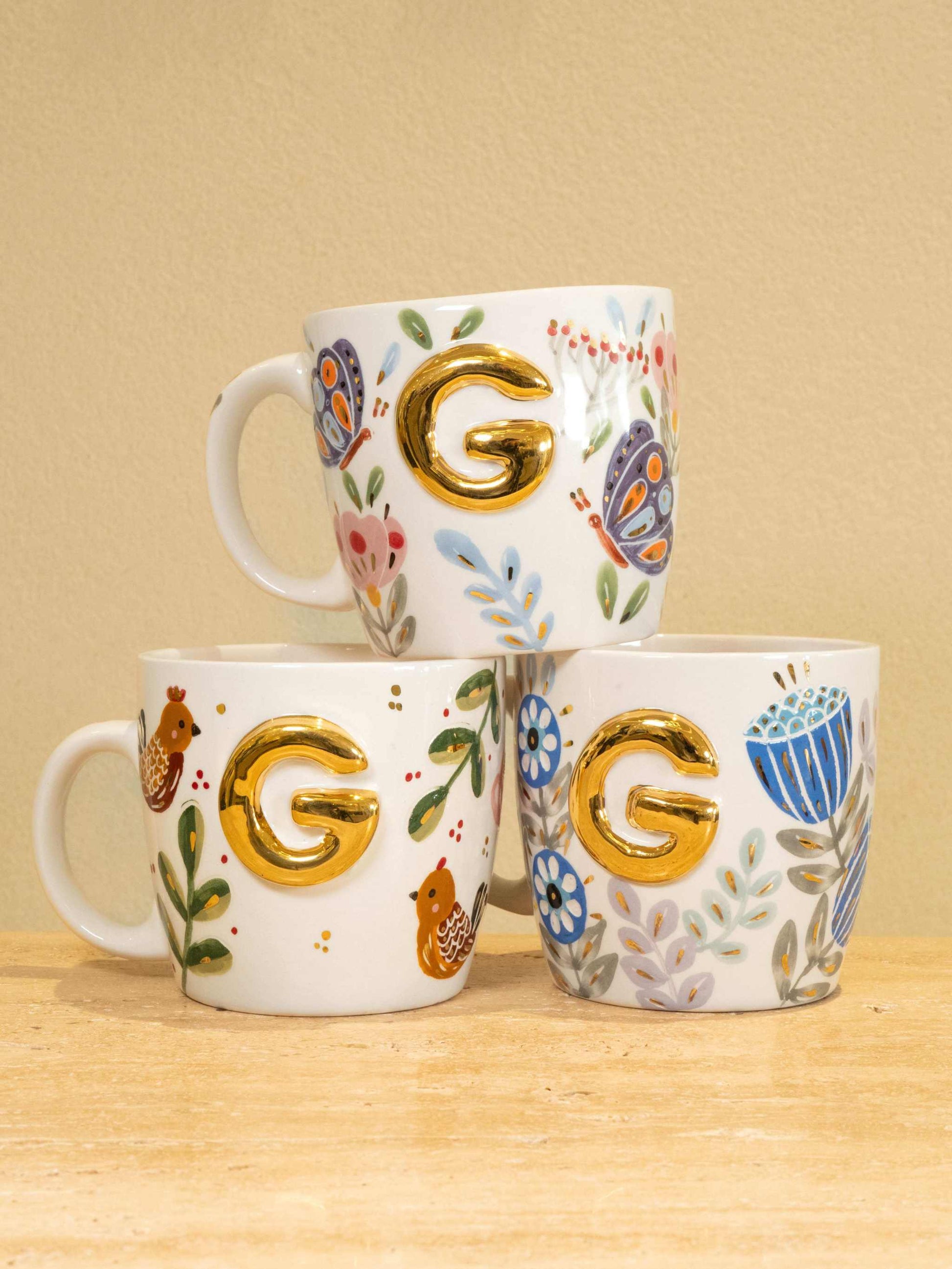 Custom handmade ceramic mugs with gold-plated initial "G" and floral design.