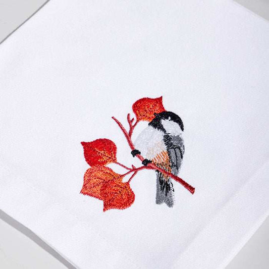 White linen cocktail napkin with embroidered bird and autumn leaves design.