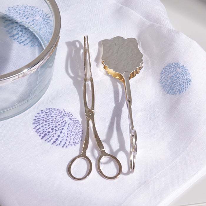Sleek silver salad tongs with polished finish on a white cloth.